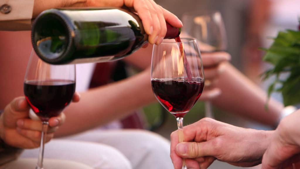 Nahaufnahme von zwei Händen, eine schenkt Cornalin aus einer Flasche in ein Weinglas, die andere hält das Glas