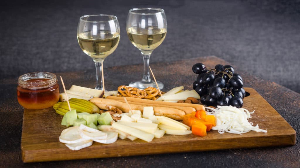 Brett mit variierter Käseplatte, Trauben, Senf und Fendant Weisswein in Gläsern.