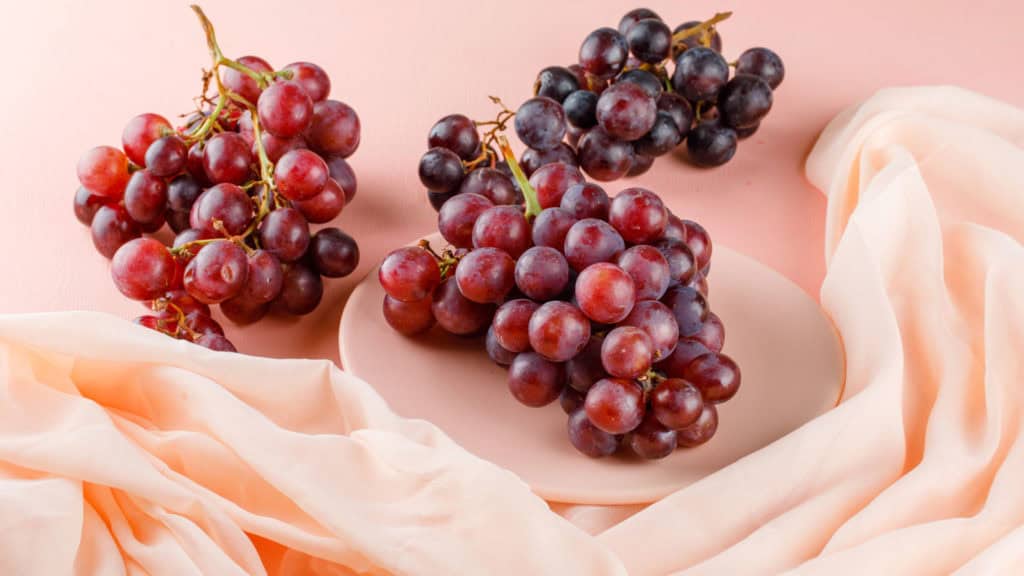 Frische Malvoisie-Trauben in Rot- und Blautönen auf einem Teller mit zartem Stoff. Perfekt für gesunde Snacks.