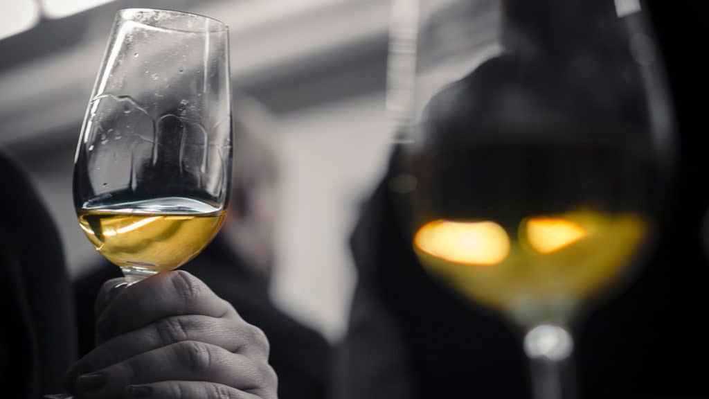 Glas mit Muscat in der Hand, verschwommene Hintergründe und weitere Gläser im Fokus.