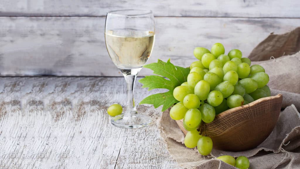 Glas Pinot Blanc-Weisswein mit Trauben – harmonische Präsentation