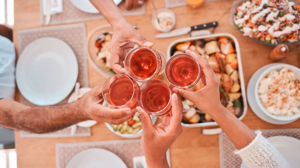 Freunde stossen mit Roséwein an, umgeben von köstlichem Essen auf einem gedeckten Tisch.