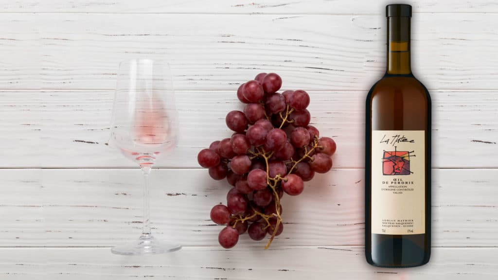 Roséwein Oeil-de-Perdrix La Matze mit roten Trauben und einem Weinglas auf Holzoberfläche.
