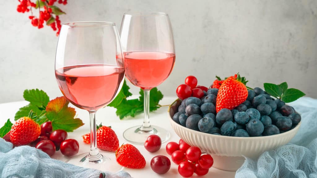 Zwei Gläser mit Roséwein und eine Schüssel mit Erdbeeren, Himbeeren und Heidelbeeren.