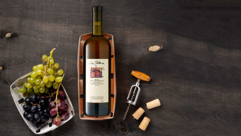 Roséwein Oeil-de-Perdrix La Matze, umgeben von Trauben, Korken und einem Korkenzieher auf einem Holztisch.