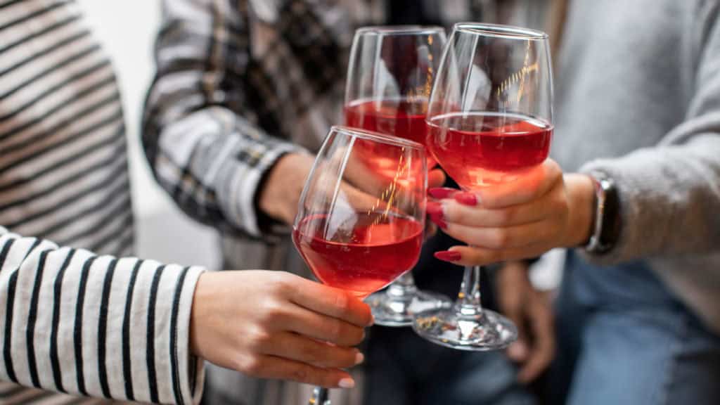 Anstossende Gläser mit Roséwein in einer geselligen Runde. Freude und Feierlichkeit sichtbar.