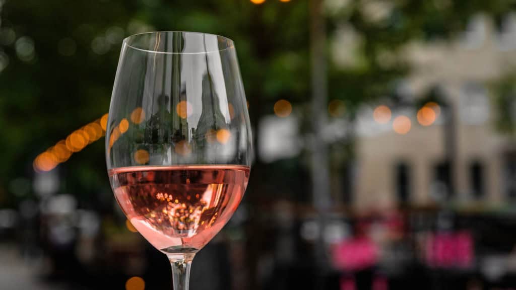 Weinglas mit Roséwein vor unscharfem Hintergrund mit Lichterketten und Gebäuden