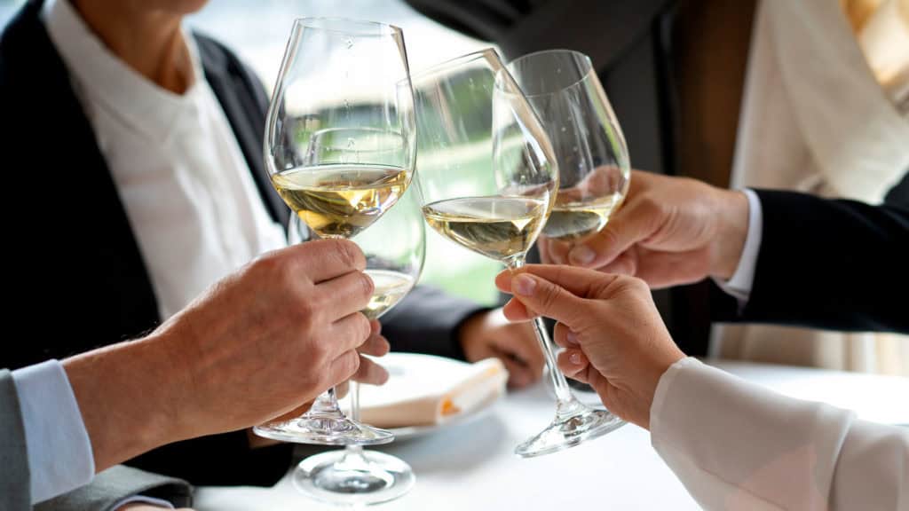 Vier Personen stossen mit Silvaner Weissweing an, im Hintergrund unscharf ein Fenster und ein Buch