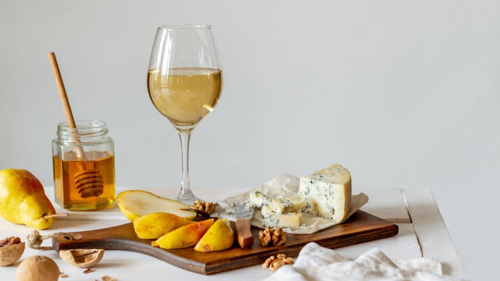 Weinglas mit Silvaner Weisswein neben Käseplatte auf Holztisch