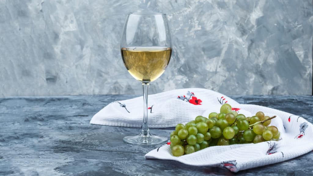 Silvaner Trauben neben Weinglas mit Weisswein, Holzuntergrund