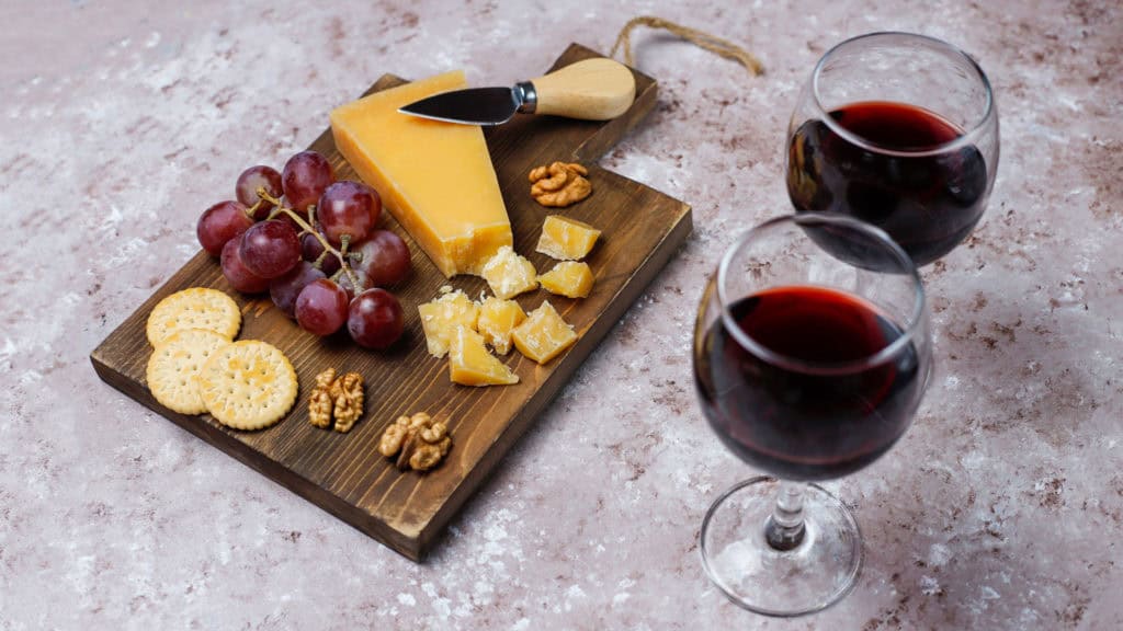 Holzbrett mit Käse, Weintrauben, Walnüssen und Crackern daneben zwei Gläser mit Syrah Wein