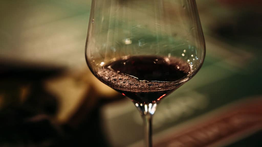 Weinglas mit Rotwein, Fokus auf Abgang, unscharfer Holztisch