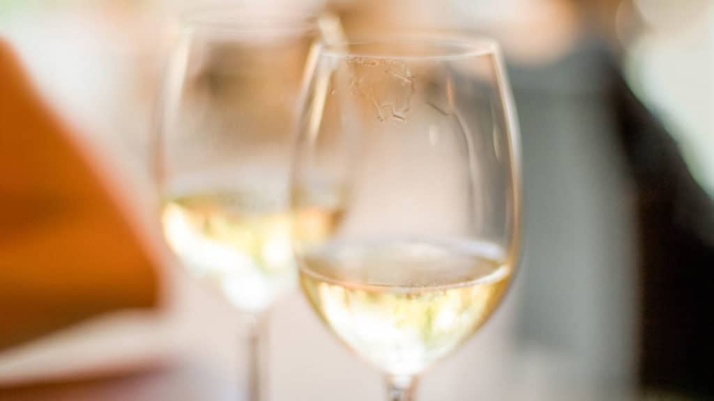 Weinglas mit Weisswein auf Holztisch, sichtbarer Abgang