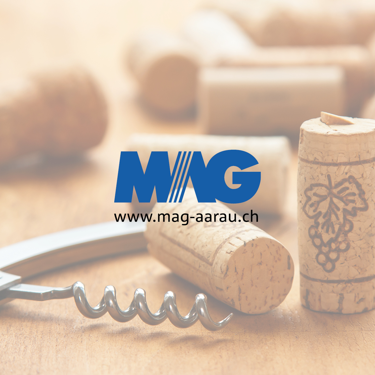 Korken mit Weintraubenmotiv und Korkenzieher auf Holztisch mit blauem Schriftzug 'MAG' und URL 'www.mag-aarau.ch'