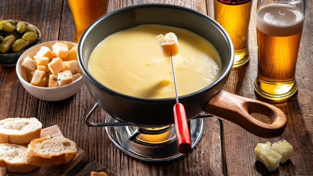 Käsefondue auf Tisch, dazu Glas Bier und Glas Wein nebeneinander
