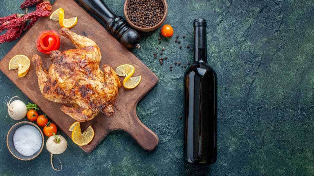 Wein & Wild: Geflügelgericht neben Rotwein im Glas, Holztisch sichtbar