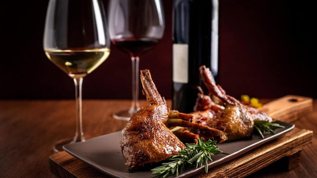 Wein & Wild: Kaninchengericht auf Teller mit zwei Weingläsern, helles Ambiente