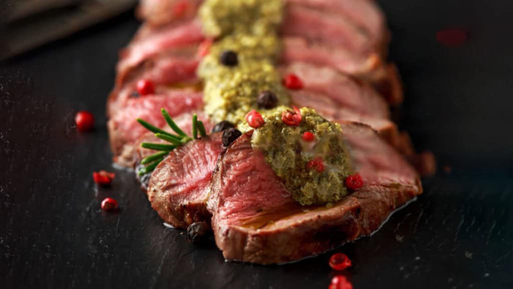 Wein & Wild: Wildschweingericht auf Teller mit Beilagen auf Holztisch