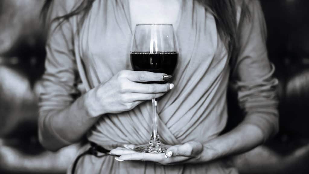 Woman holding a red wine glass with both hands in front of her upper body. Focus on the final finish 