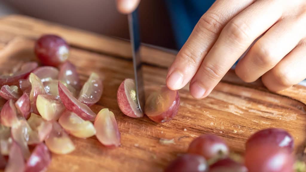 Frau schneidet frische Weintrauben auf einem Holzbrett, Vorbereitung für Wein und Nährstoffaufnahme