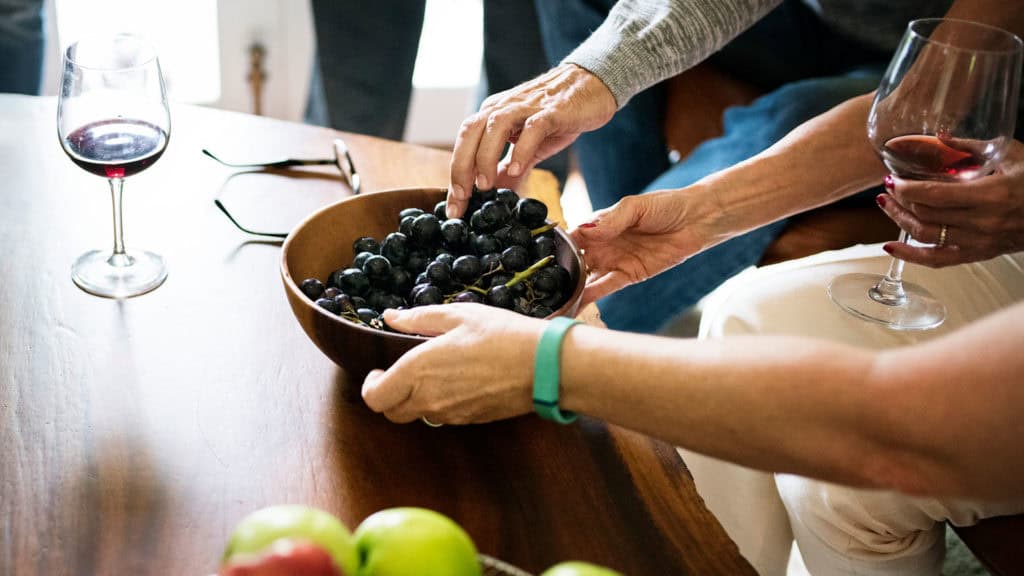 Altere Menschen geniessen Wein, daneben ein Weinglas und Trauben, Hinweis auf gesundheitsfordernde Inhaltsstoffe