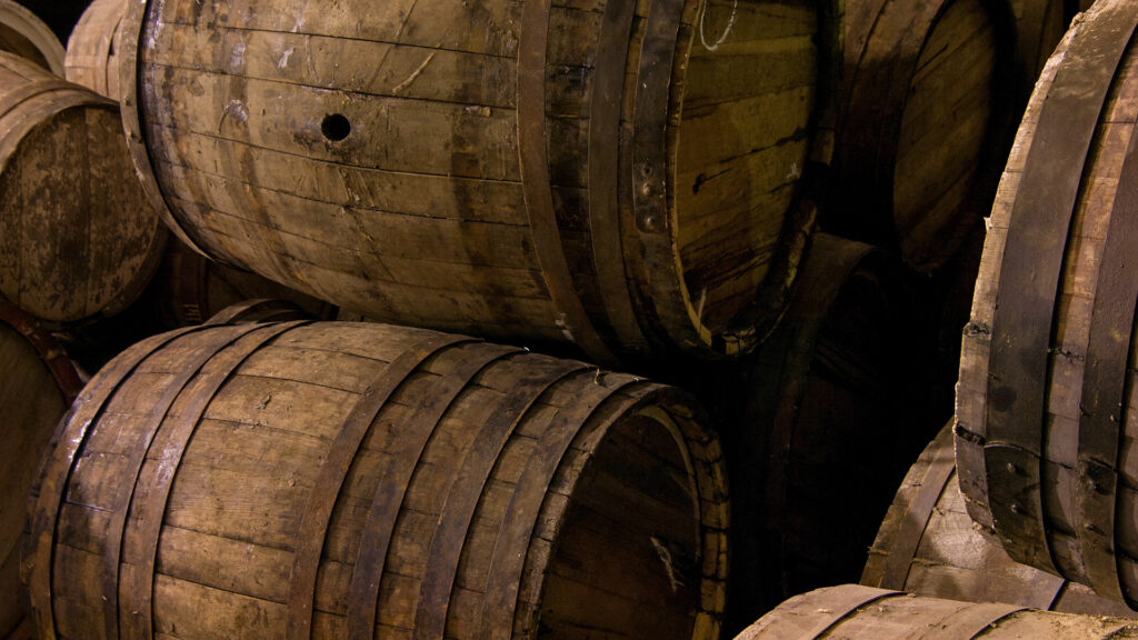 Mehrere alte Barrique-Eichenholzfässer mit Metallreifen, übereinander gestapelt in einem dunklen Lagerraum