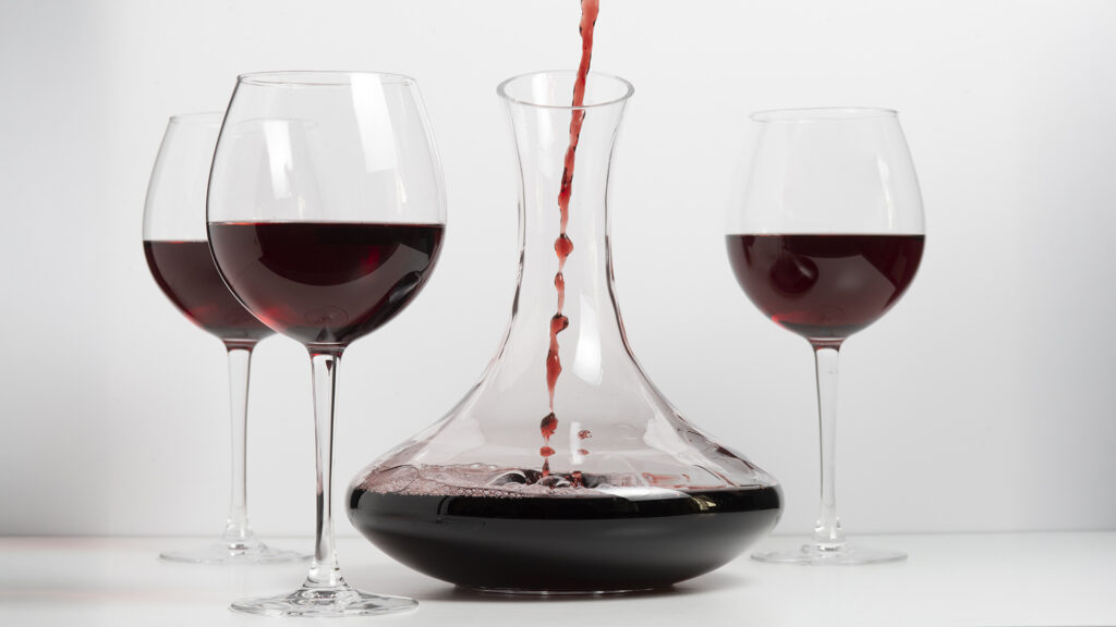 Rotwein wird ins Dekanter gegossen, Fokus auf Dekantieren, heller Hintergrund