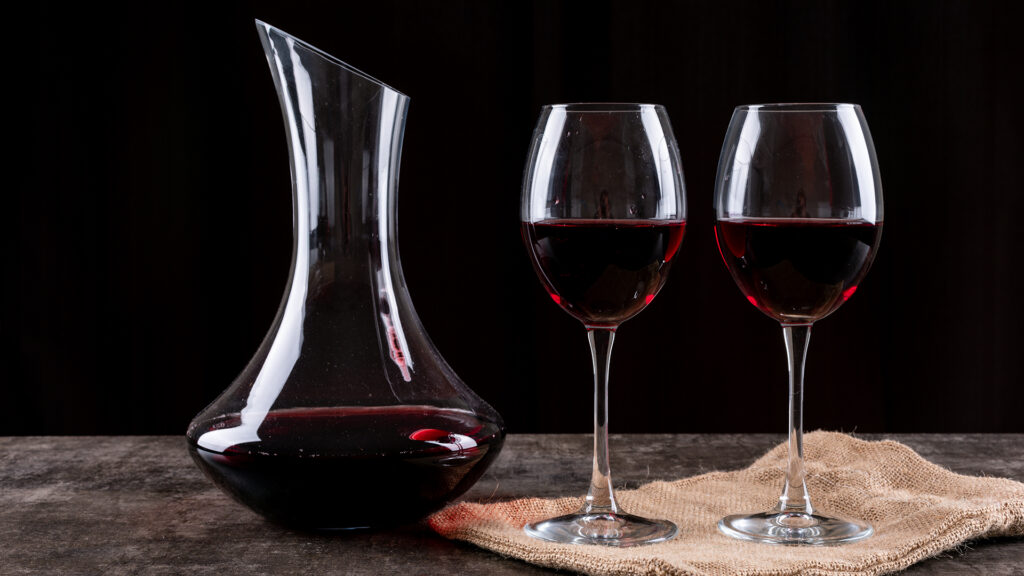 Dekanter mit Rotwein auf Tisch, daneben zwei Rotweingläser, Dekantieren im Mittelpunkt