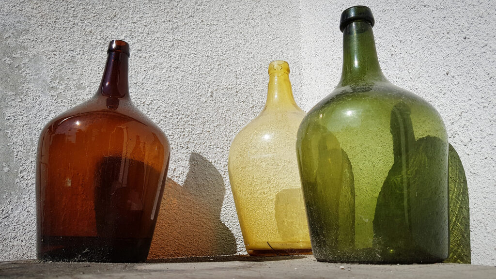 Drei grosse Flaschengrössen in Braun, Gelb und Grün stehen vor einer weissen Wand