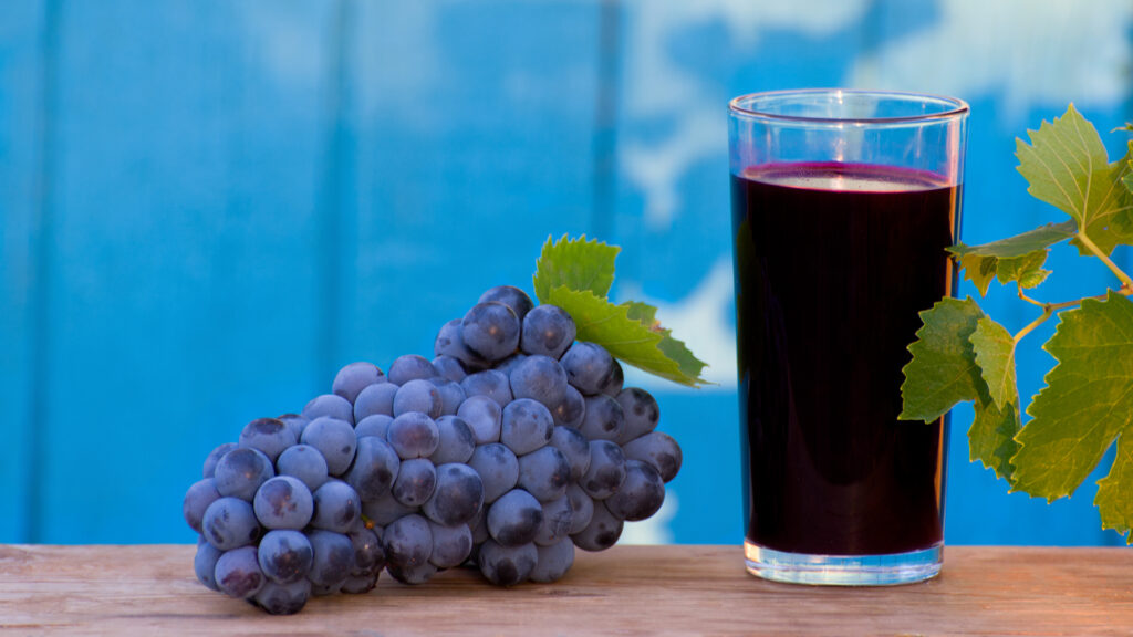 Jus de raisin non fermenté dans un verre à côté d'une grappe de raisin et de feuilles de vigne sur une table en bois sur fond bleu.
