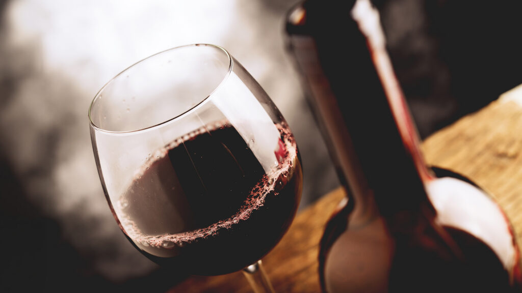 Weinglas mit Grand Cru Wein neben einer geöffneten Weinflasche auf einem Holztisch