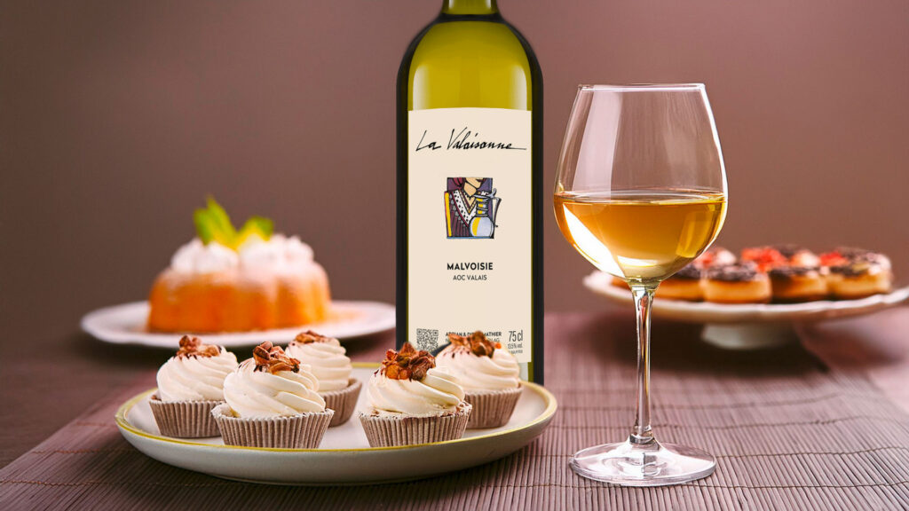 Weisswein La Valaisanne Malvoisie in Flasche, Glas und dekadente Desserts auf einem Tisch.