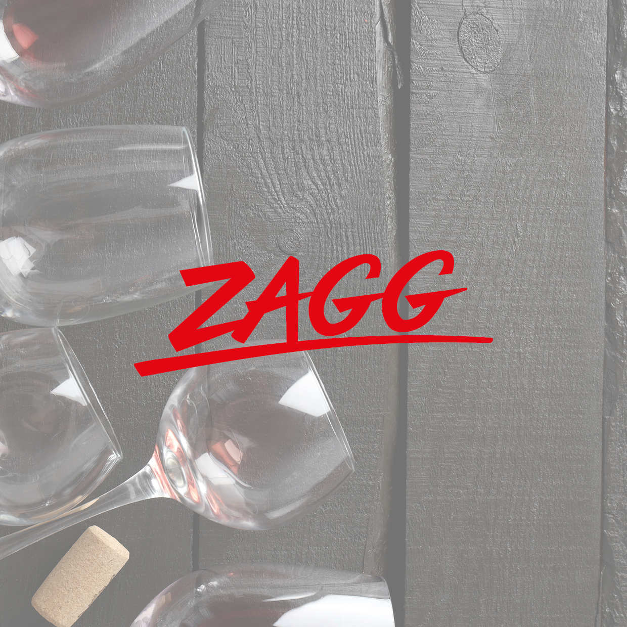 Mehrere Weingläser und ein Korken liegen auf einer Holzoberfläche mit rotem Schriftzug 'ZAGG'