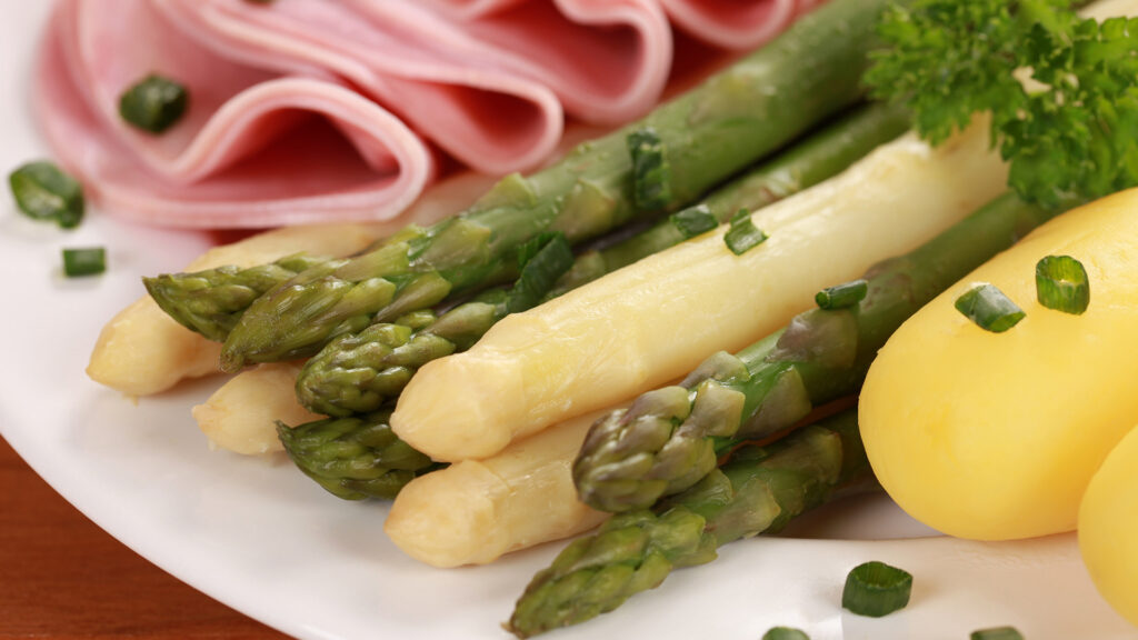 Thema Weine zu Spargel: Grüne und weisse Spargelstangen mit gekochtem Schinken, Petersilie und Kartoffeln auf weissem Teller